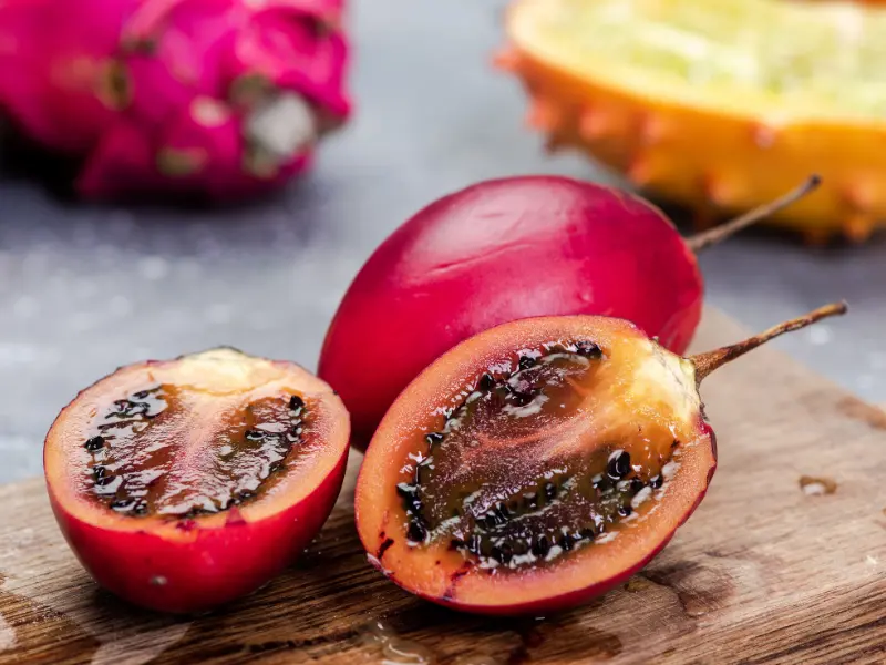 A cross-section of a fresh red tamarillo showing the dark seeds and succulent pulp on a wooden cutting board.